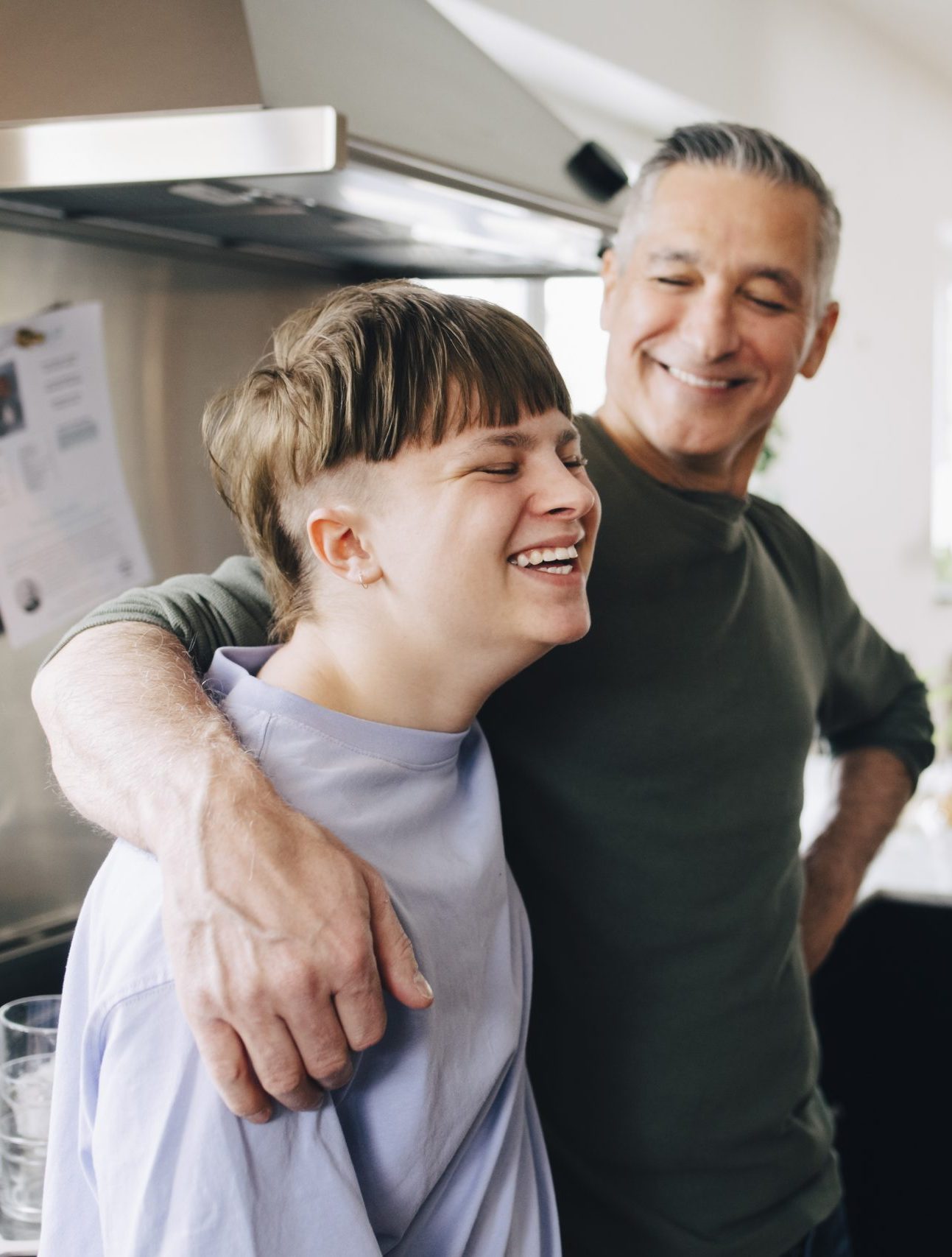 male foster carer with arm around happy fostered child in the kitchen